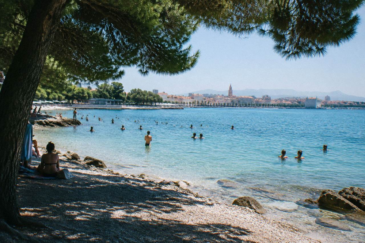 Swimmers in clear turquoise water at a pebble beach on the Adriatic coast near Split