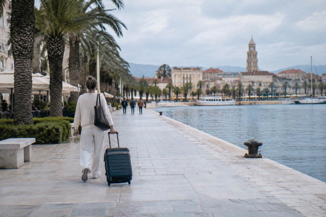 Passenger walking with a suitcase along the sunny waterfront promenade in Split