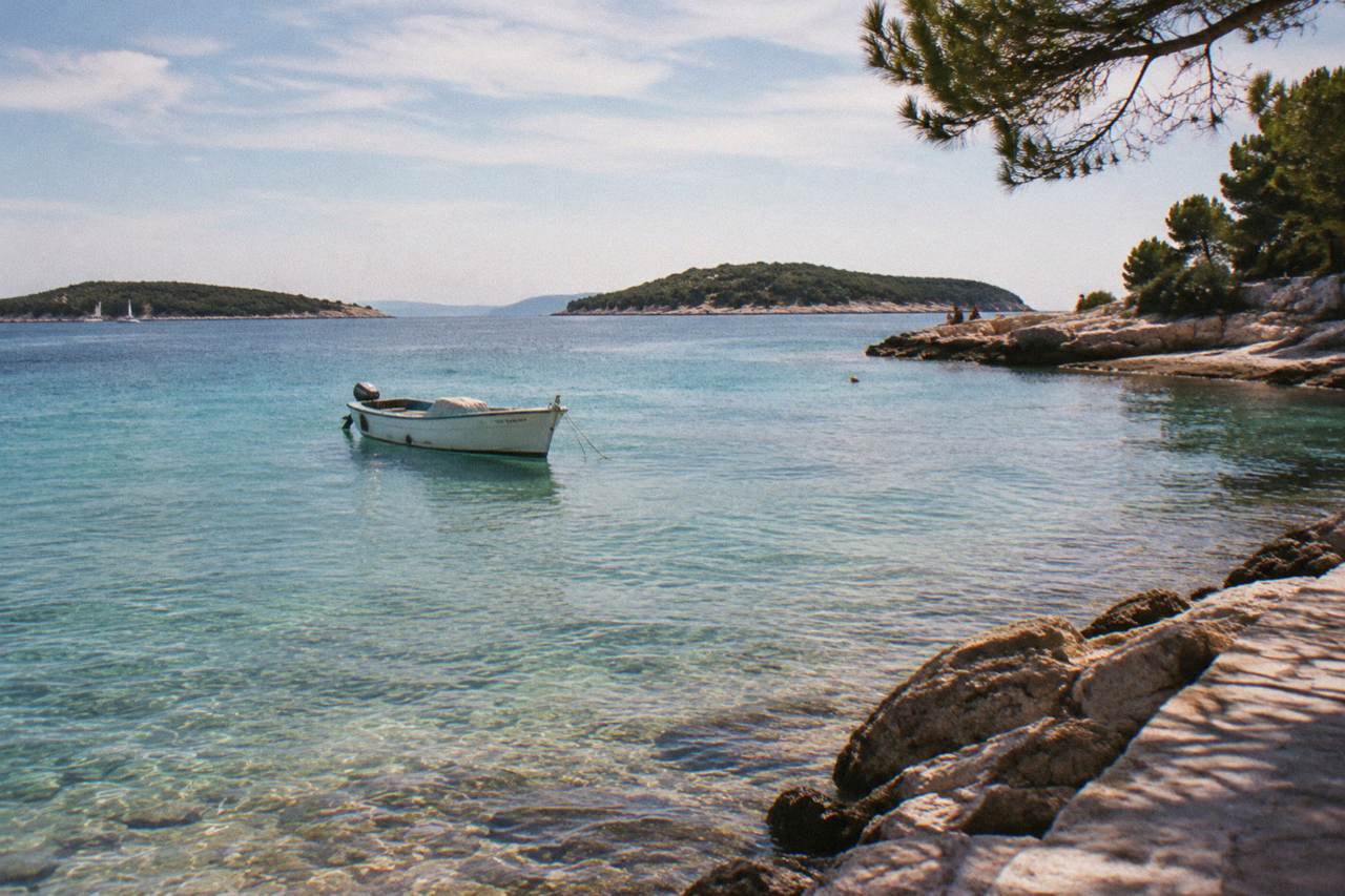 A small boat anchored in a shallow turquoise cove between Dalmatian islands on a calm summer morning