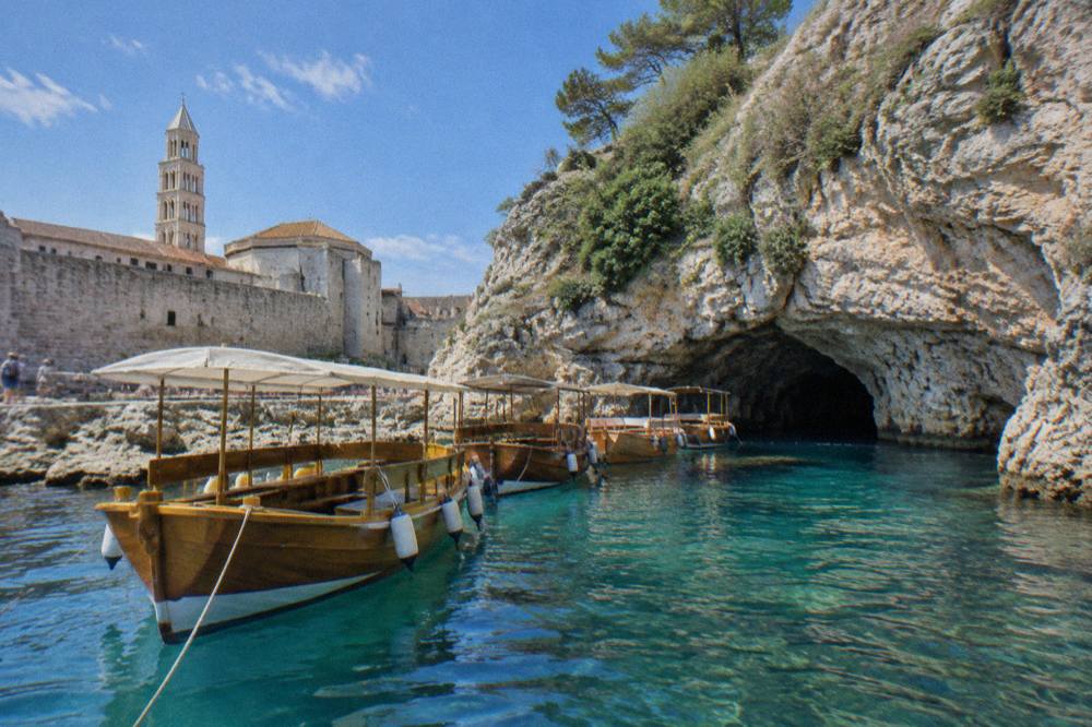 Wooden transfer boats lined up outside a low sea cave entrance on a rocky island coast