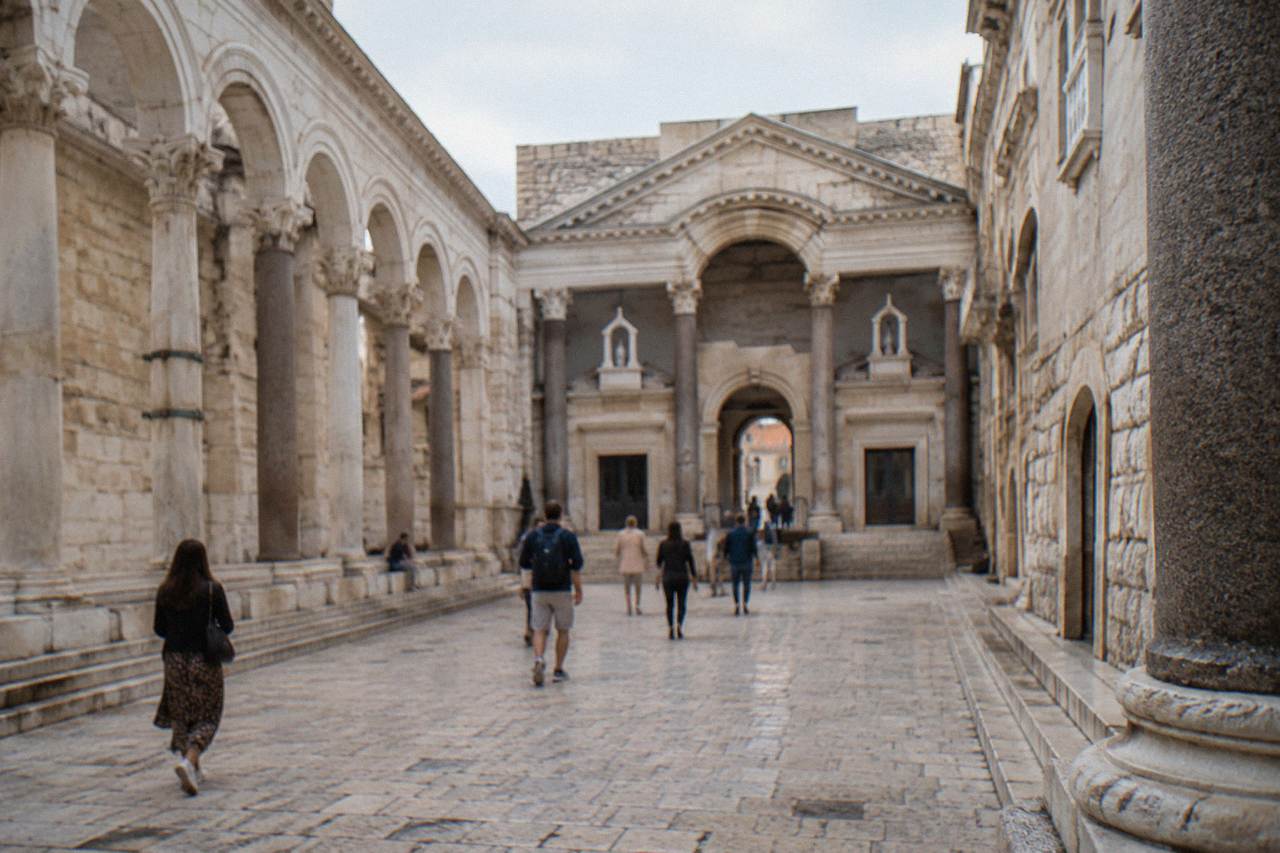 Sunlit stone courtyards and arcades inside Diocletian's Palace in Split with visitors walking through