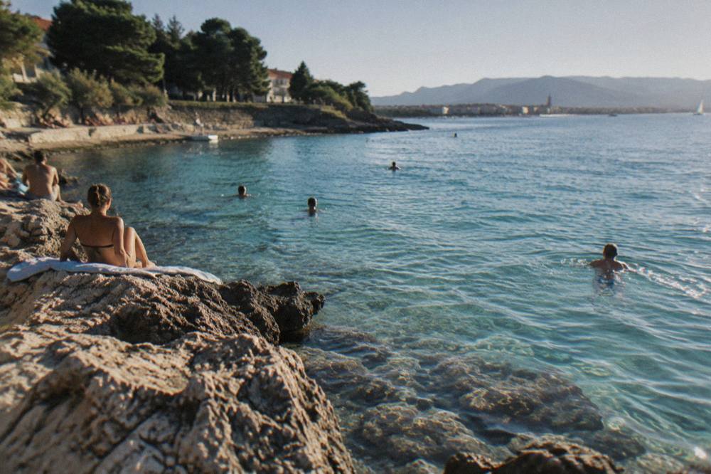 Swimmers in clear turquoise water beside a rocky shoreline on a Dalmatian island