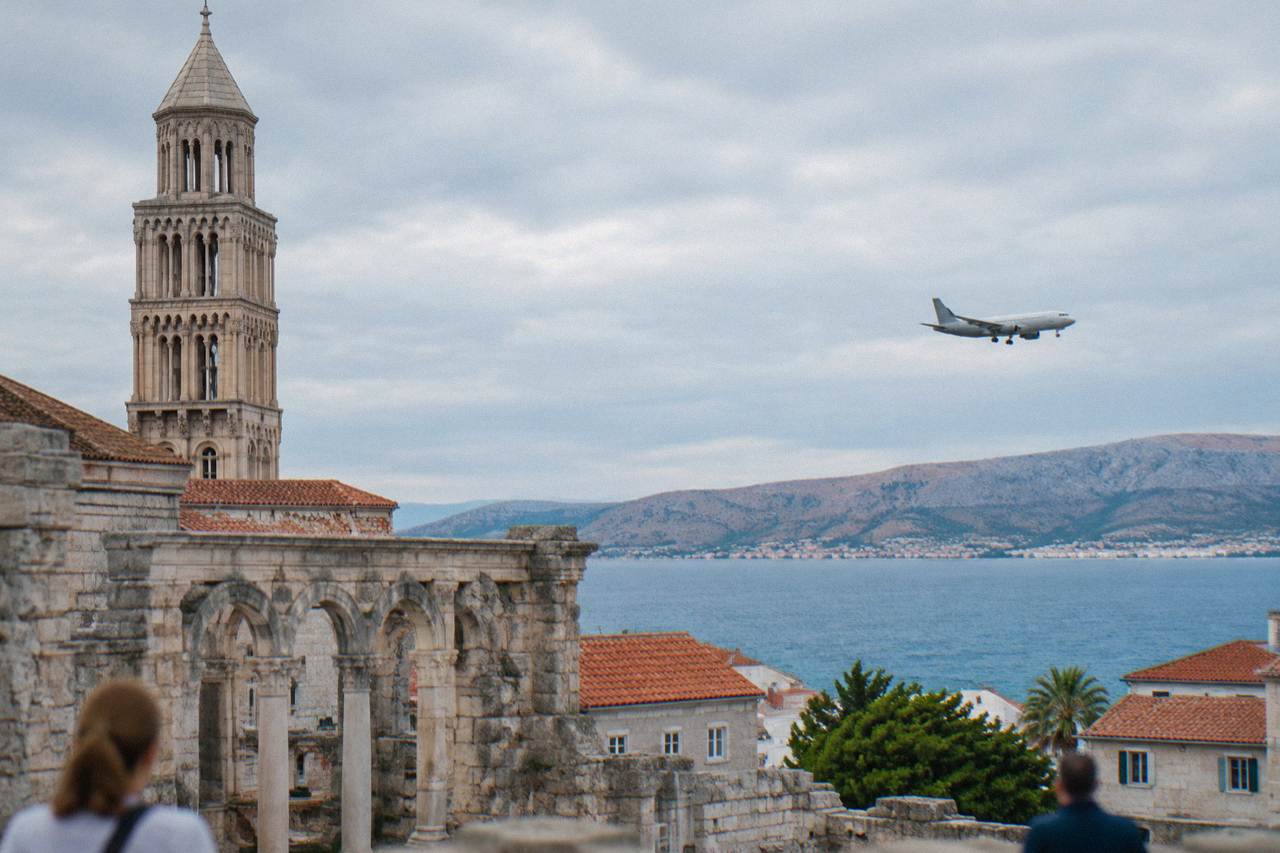 A passenger plane descending over the Adriatic coast near Split with dry hills and a blue sea below