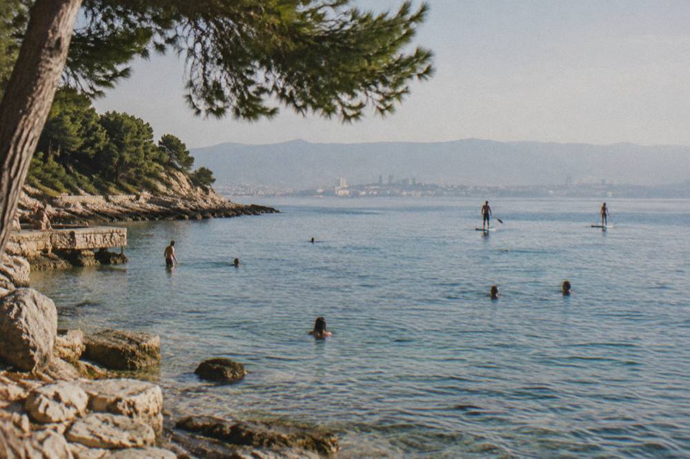 Swimmers and paddleboarders in the shallow water at a stone beach on the Marjan peninsula in Split