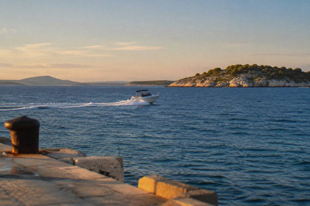 A speedboat crossing open blue sea toward rocky islands off the Split coastline in bright afternoon light
