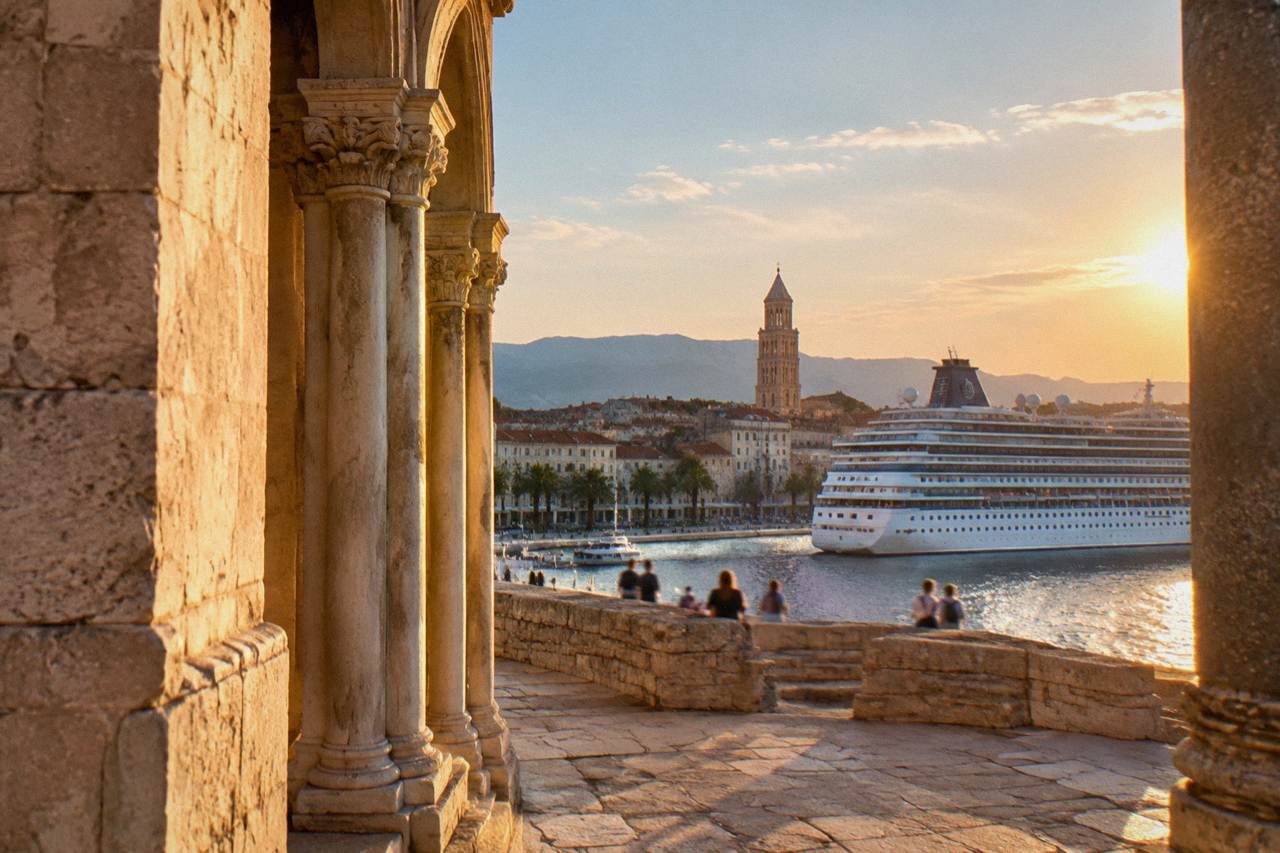 A cruise ship moored at the Split waterfront with the bell tower of the old town rising behind it