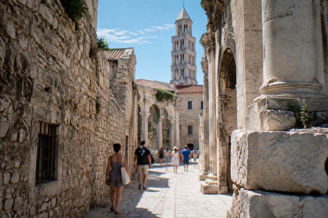 A stone alley inside Diocletian's Palace in Split with visitors in summer clothing walking past old walls