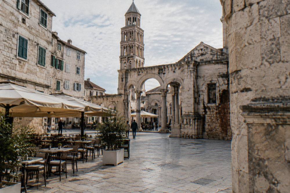 A stone-paved square in an old Dalmatian town with cafe tables and shuttered facades