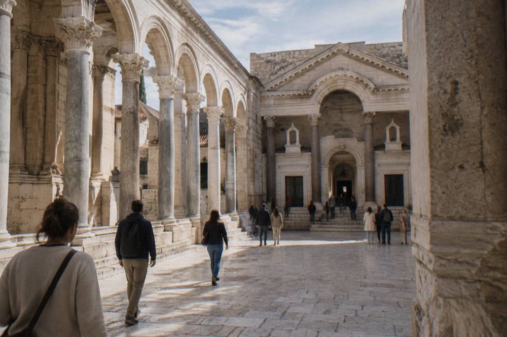 Visitors walking through the colonnaded Peristyle courtyard of Diocletian's Palace in sunlight