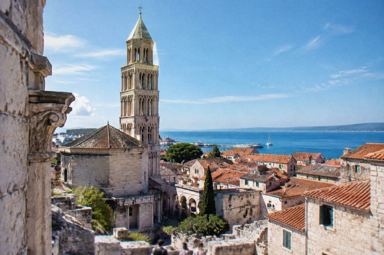 The stone walls and bell tower of Diocletian's Palace rising above the rooftops of Split with the Adriatic Sea in the distance