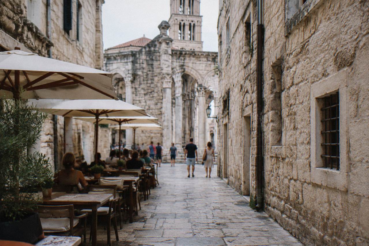 A narrow stone street inside Diocletian's Palace in Split with café tables and pedestrians in summer light.