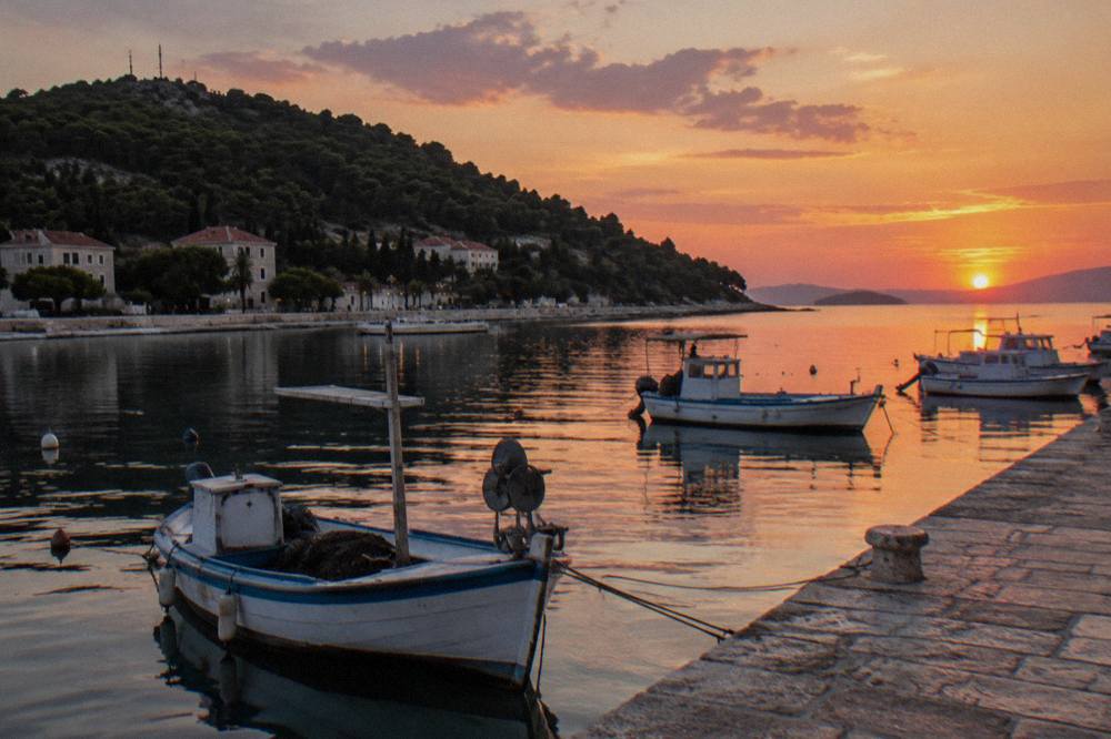 Fishing boats and a stone quay on the Split waterfront at dusk with the Marjan hillside behind.