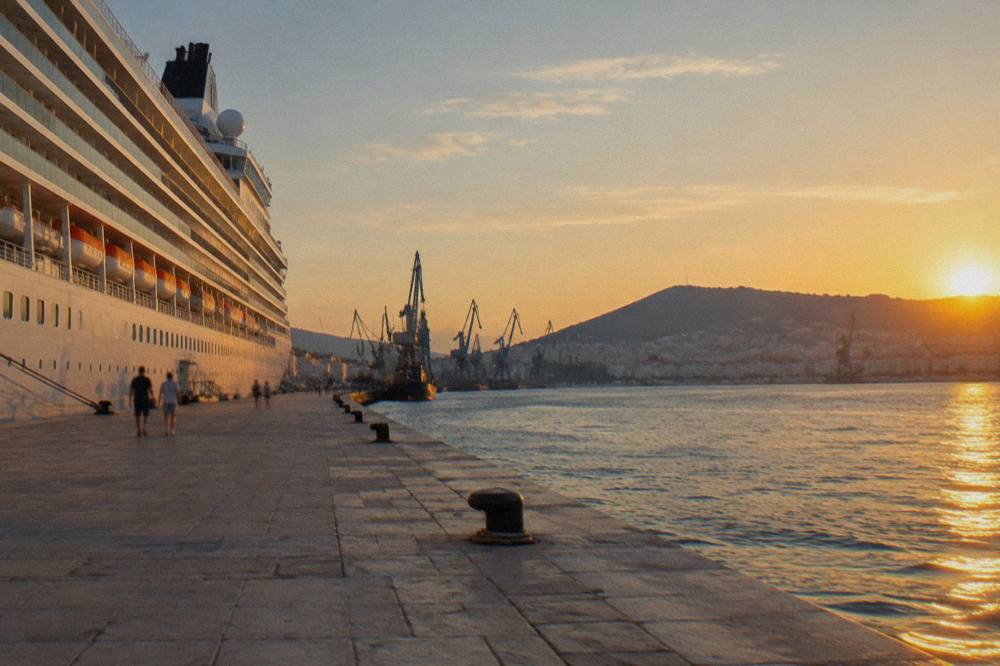 A large cruise ship alongside a long quay in Split port with cranes and the harbour hills beyond