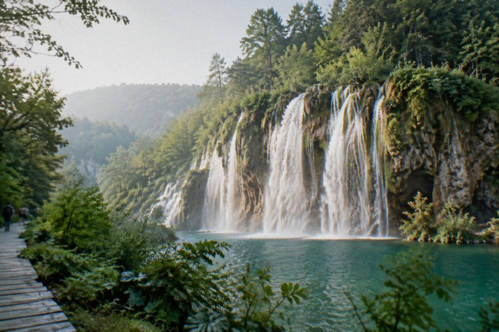 Broad waterfall spilling over travertine barriers into a pool ringed by green forest