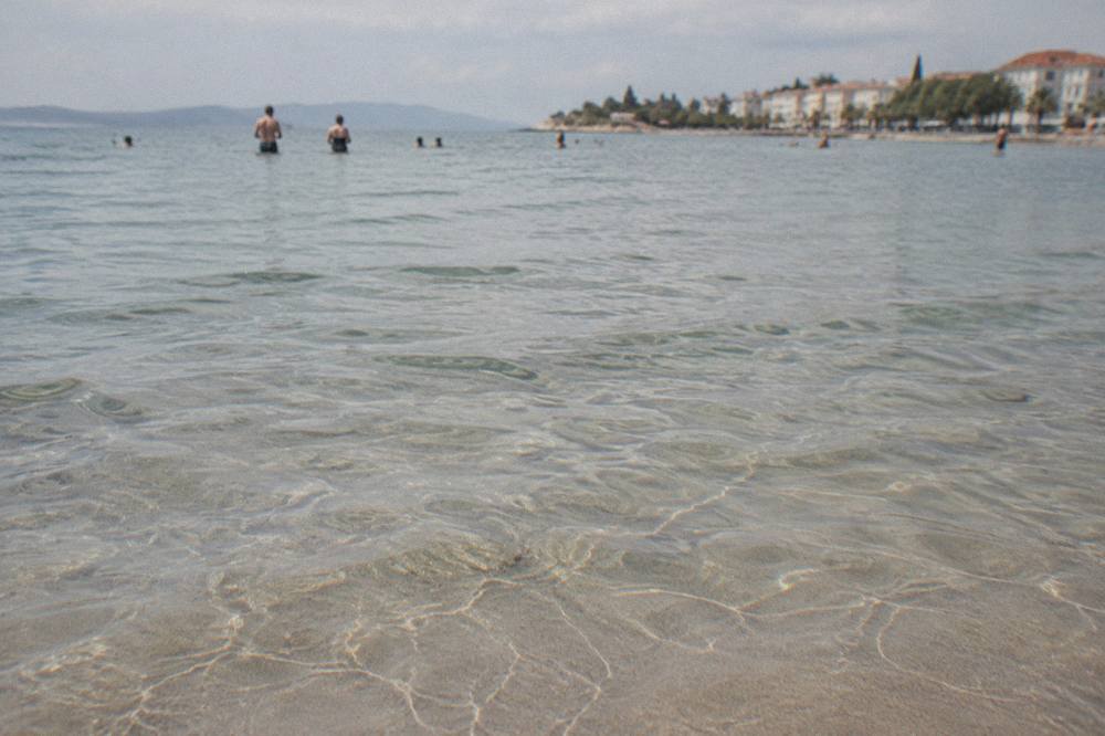 Clear shallow water over sand with feet visible and morning light