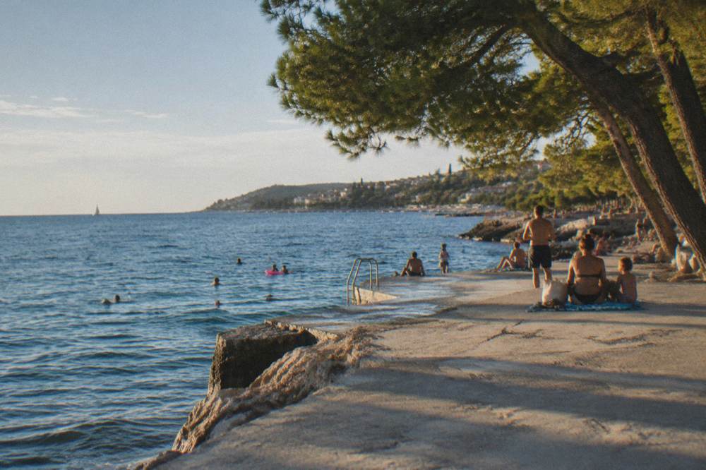Families on a flat concrete swimming platform beside pine trees at Stobrec
