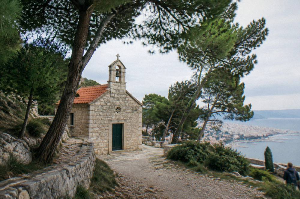 Small stone church with a simple bell facade among pine trees above Split