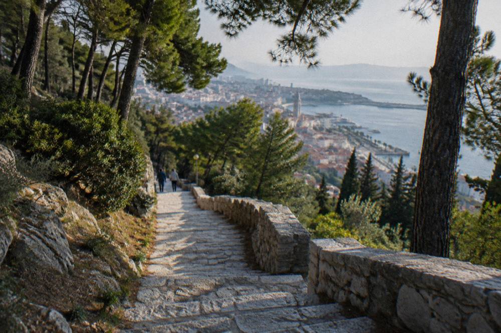 Stone staircase climbing through pine forest toward a viewpoint above Split