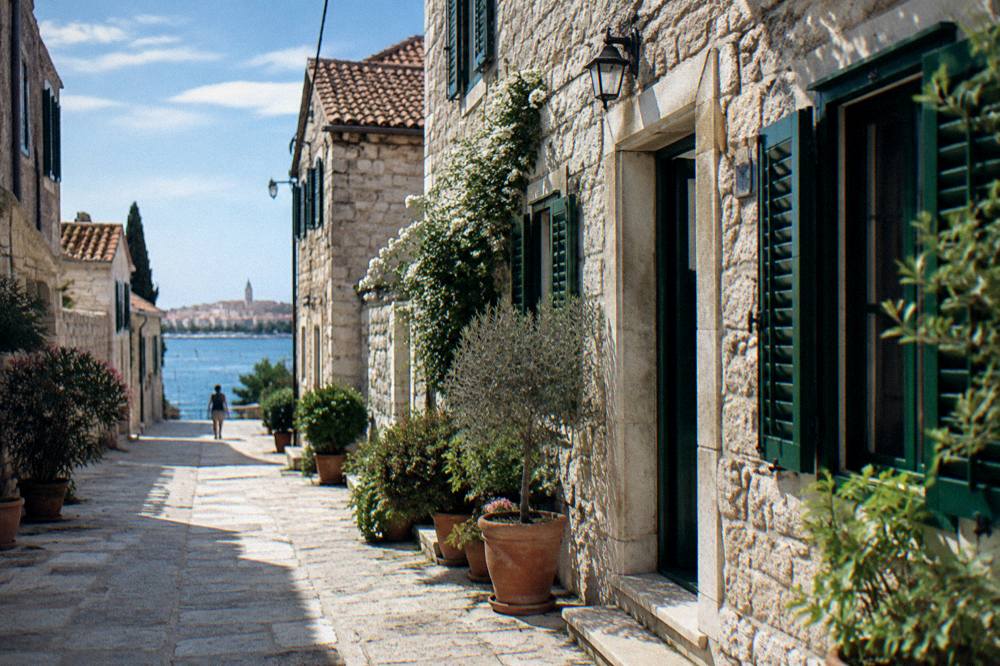 Quiet stone street in Veli Varos with green shutters and potted plants in soft morning light