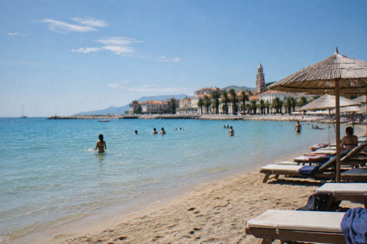 Sandy city beach with shallow turquoise water and sunloungers under parasols