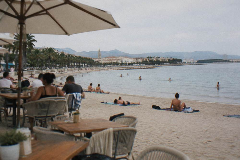 Beach cafe terrace with tables on the sand behind sunbathers