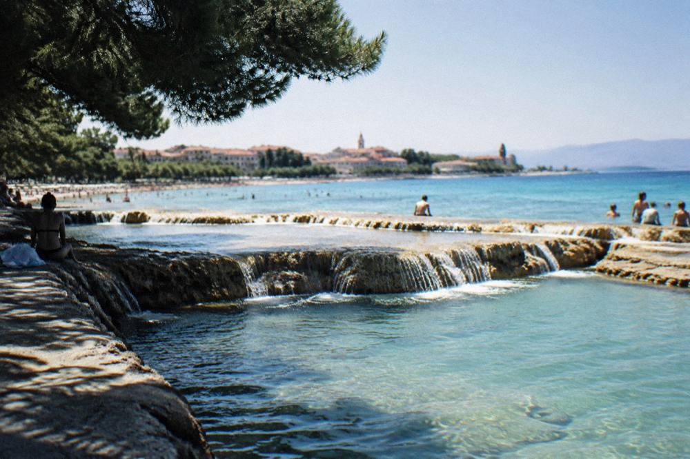 Turquoise river water spilling over travertine barriers into a pool