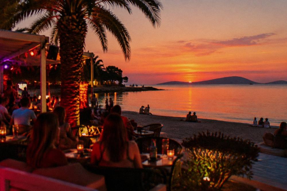 Lit nightclub terrace on the sand with people at tables after sunset