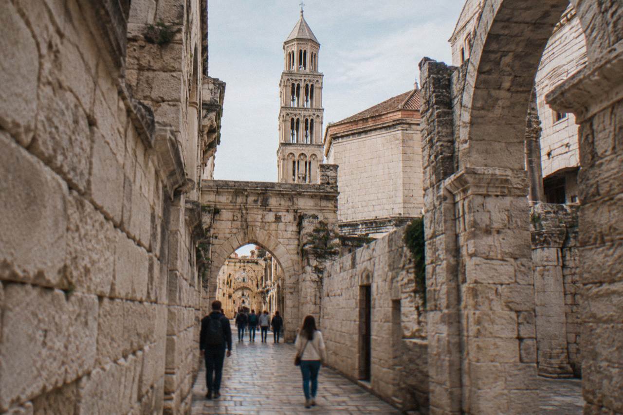 Ancient stone walls and arches of Diocletian's Palace in Split with people walking through a narrow lane