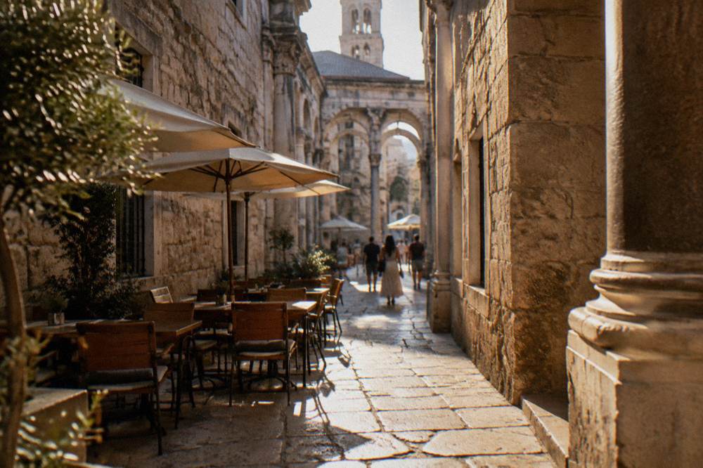 Sunlit stone lane inside the old palace with cafe tables and shoppers in the morning