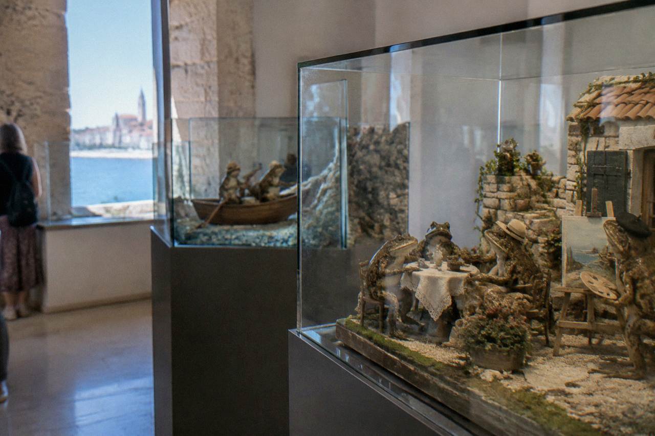 A small museum room with glass display cases of taxidermied frogs arranged in miniature human scenes