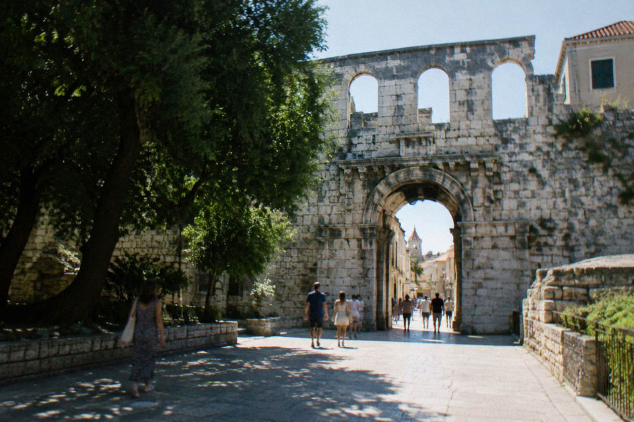 The stone north gate of Diocletian's Palace in Split with people walking through the archway