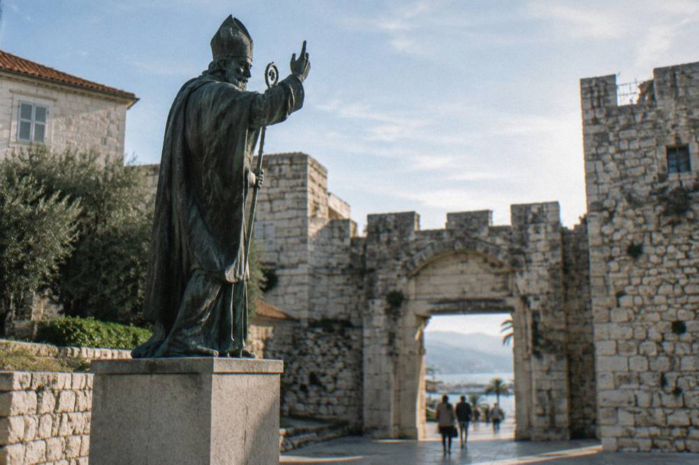 A large bronze statue of a bishop raising a hand, standing on a pedestal outside the Golden Gate in Split