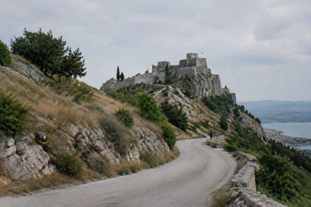 A winding road climbing through dry hills toward a fortress on a ridge