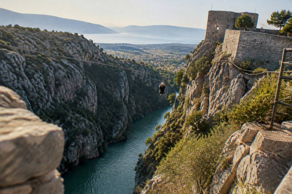 A river canyon with steep rocky walls and green water below a zipline