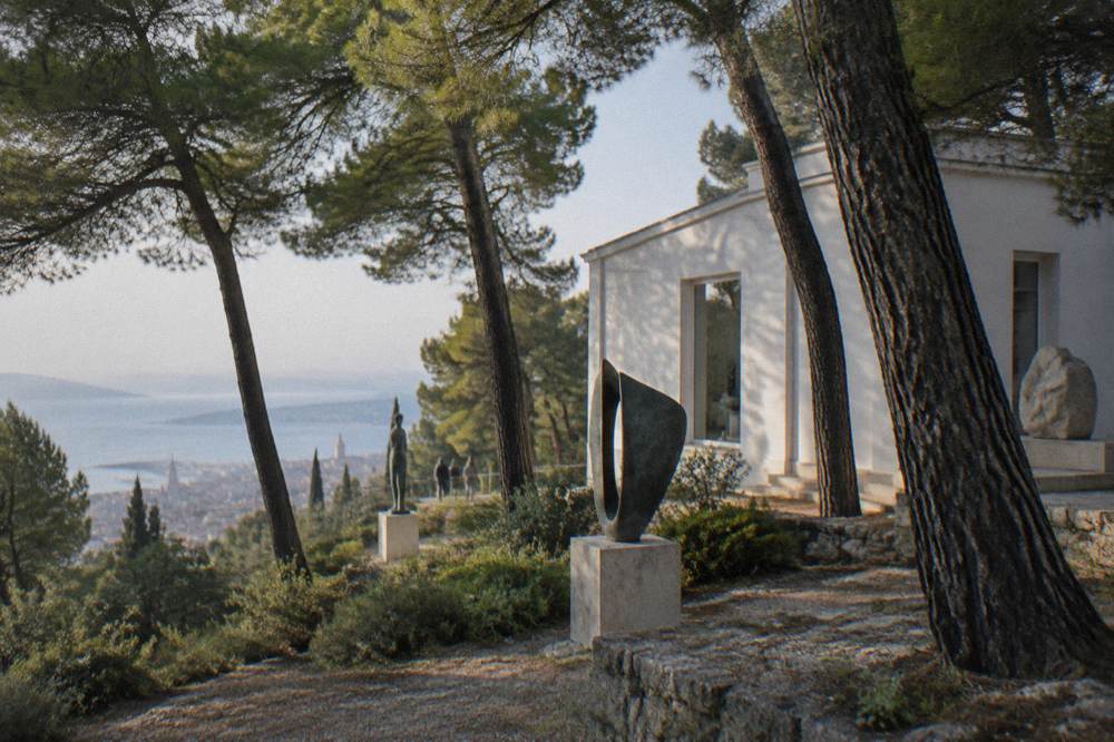 A white gallery building surrounded by pine trees and sculpture on the slope of Marjan hill