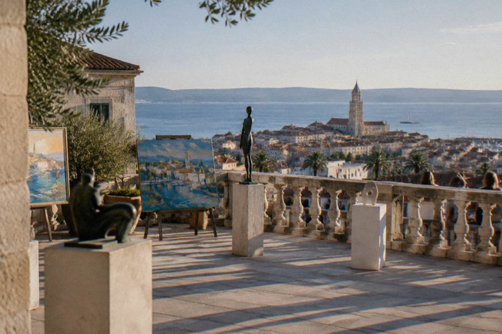 A sunlit gallery terrace with a stone balustrade overlooking the sea