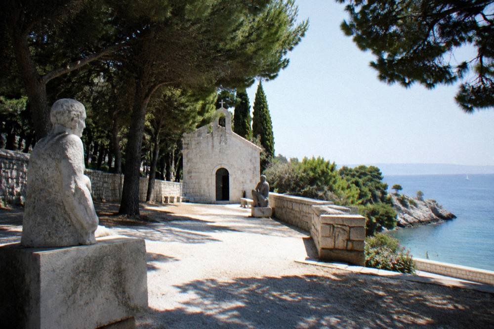 A walled stone chapel courtyard above a small cove on the Split coastline