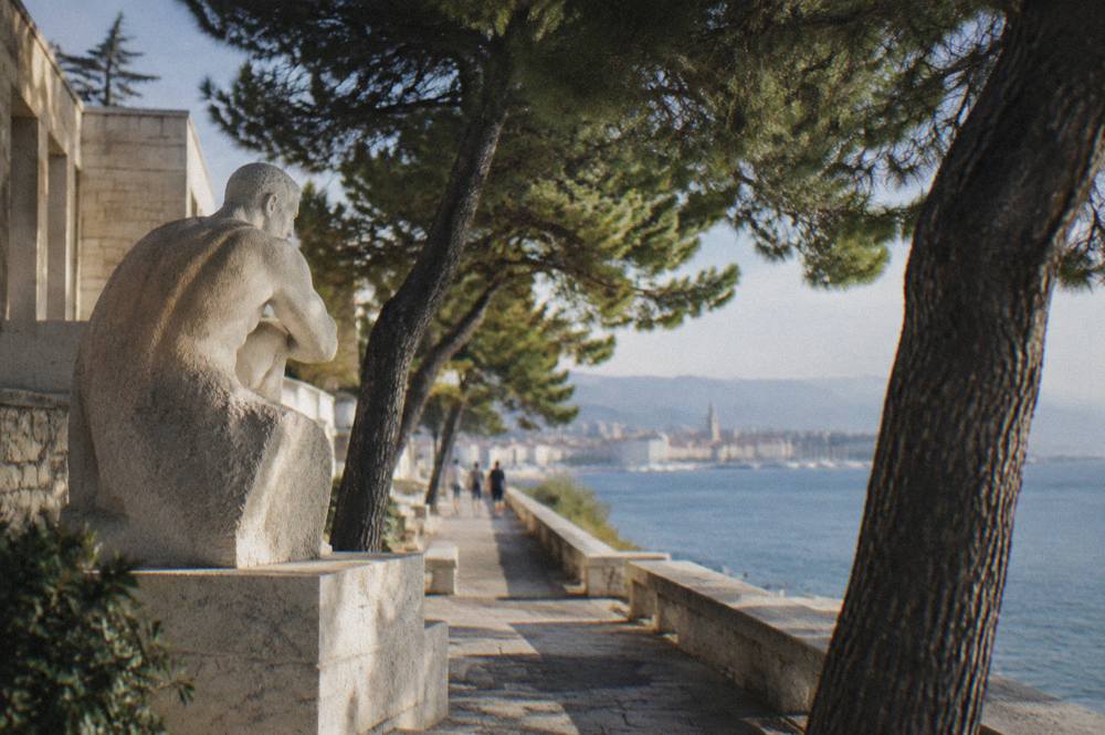 Pine trees shading a seaside promenade on a warm afternoon in Split