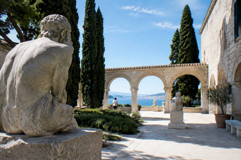 A walled Renaissance-style courtyard with stone arches and cypress trees near the Split seafront