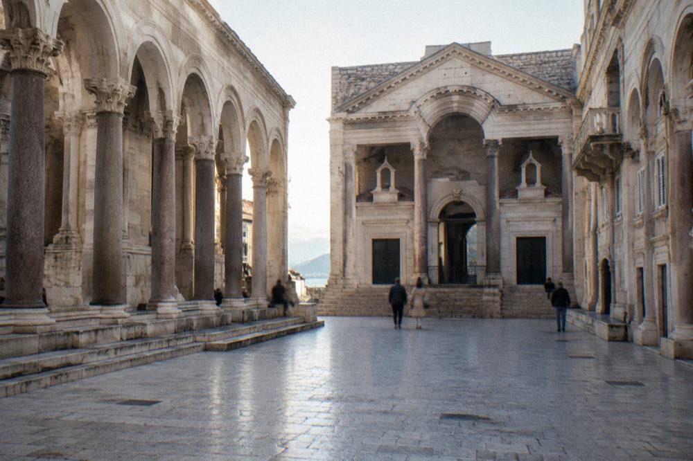 A broad stone square with neoclassical arches and a church facade at one end