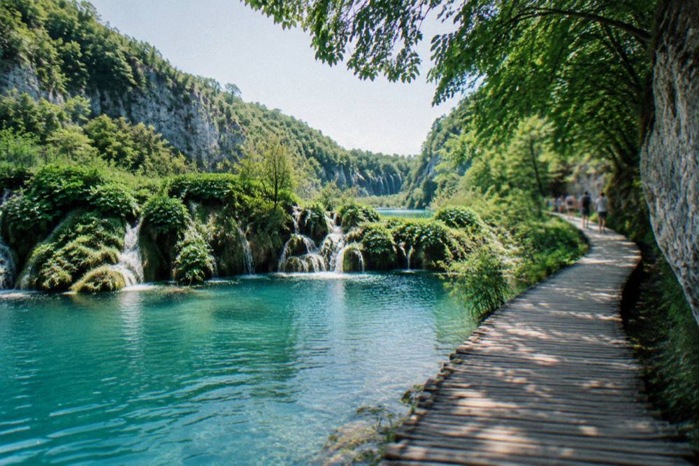 A wooden walkway crossing a series of turquoise lakes with waterfalls between forested cliffs