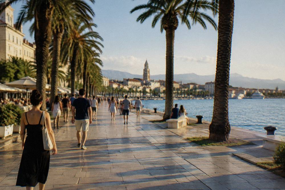 People strolling under palm trees on the seafront promenade in late afternoon light
