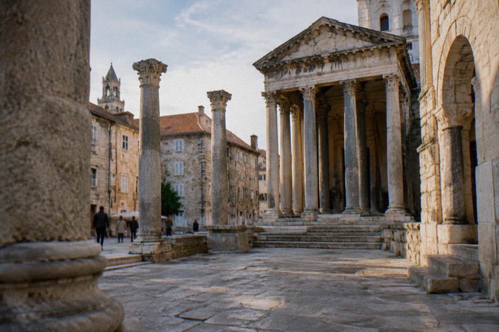 A colonnaded ancient square with stone columns and buildings under warm light