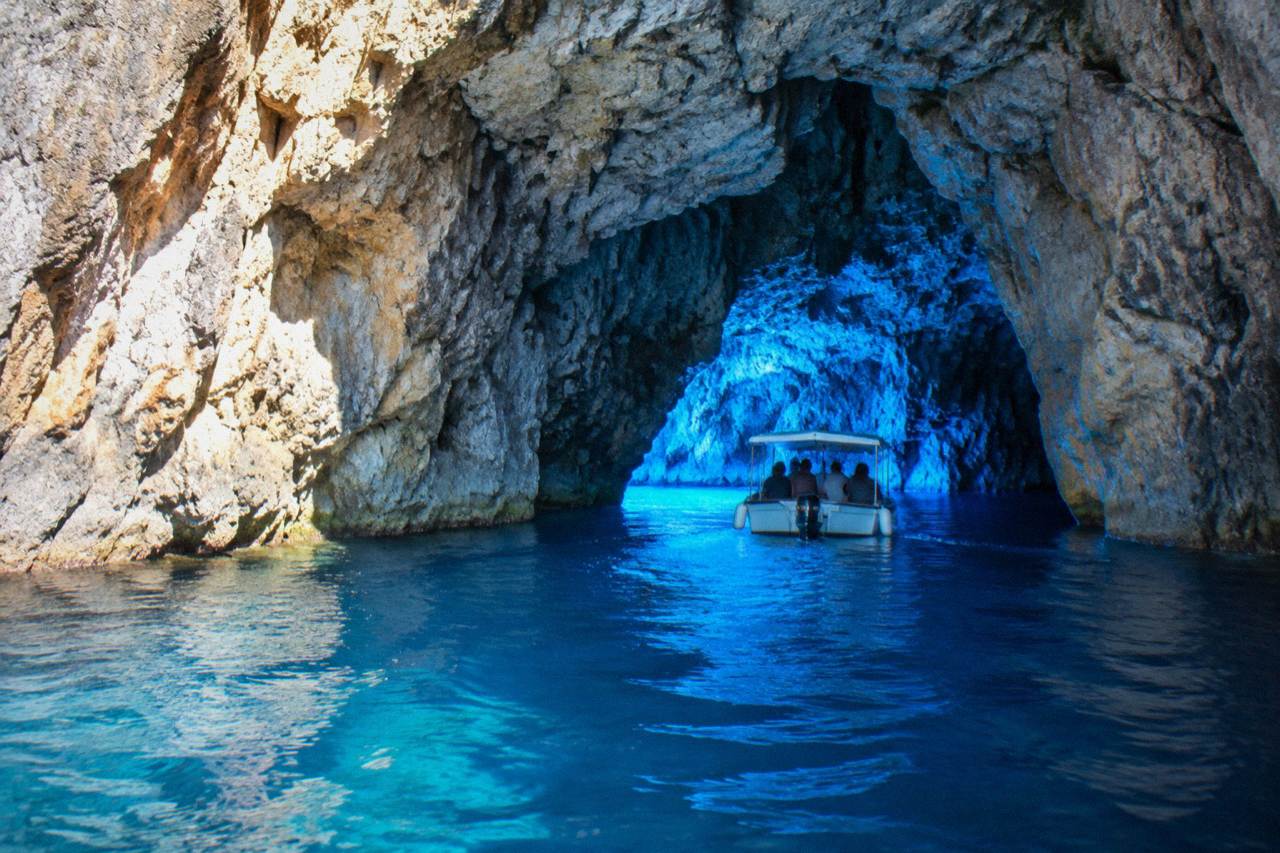 A small boat entering a glowing blue sea cave on a sunny morning