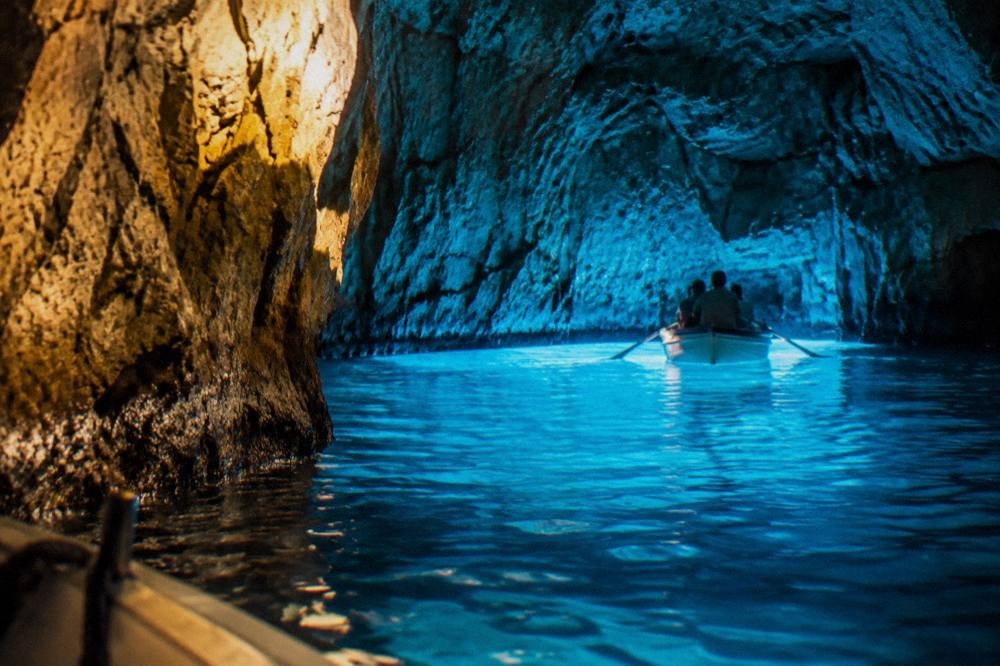 Turquoise light filling the inside of a sea cave with a small rowing boat inside