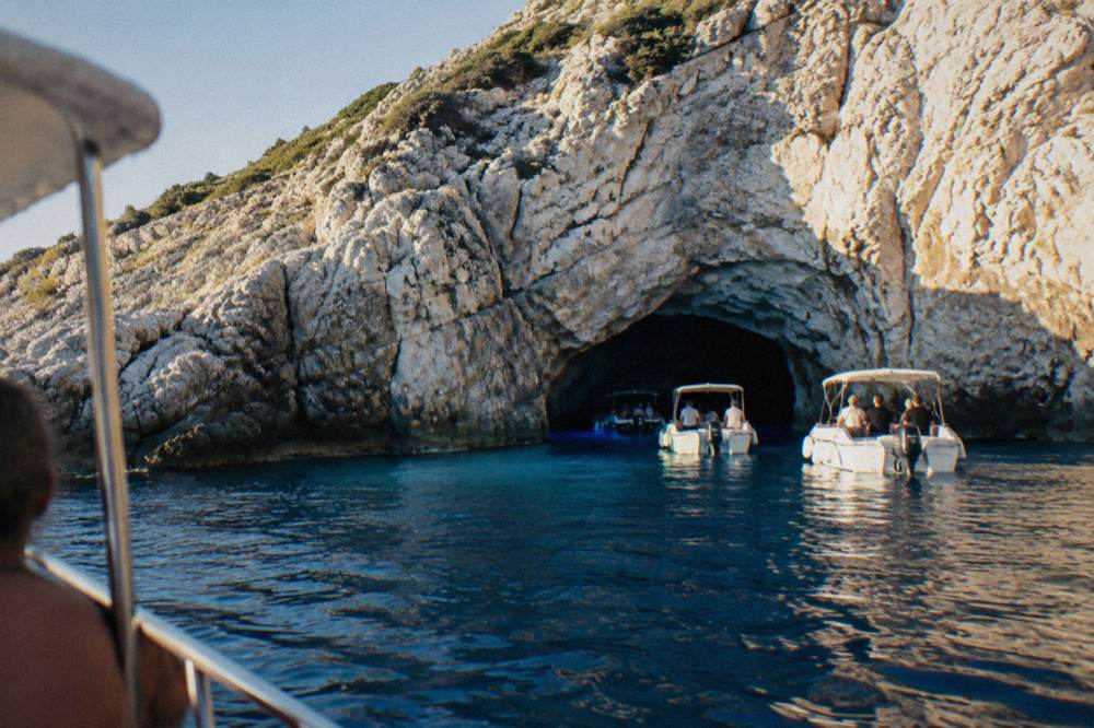 Boats waiting outside a white limestone cave entrance on a rocky island shore