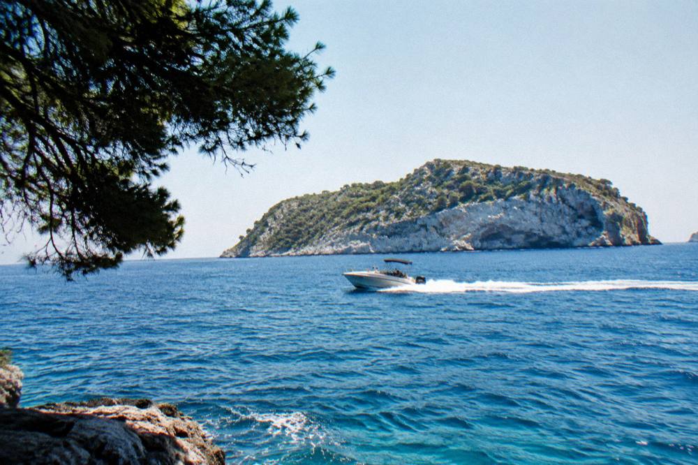 A speedboat cutting across open blue sea with a rocky island ahead