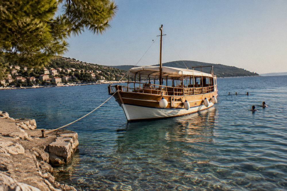 A wooden tour boat moored in clear shallow water with swimmers nearby