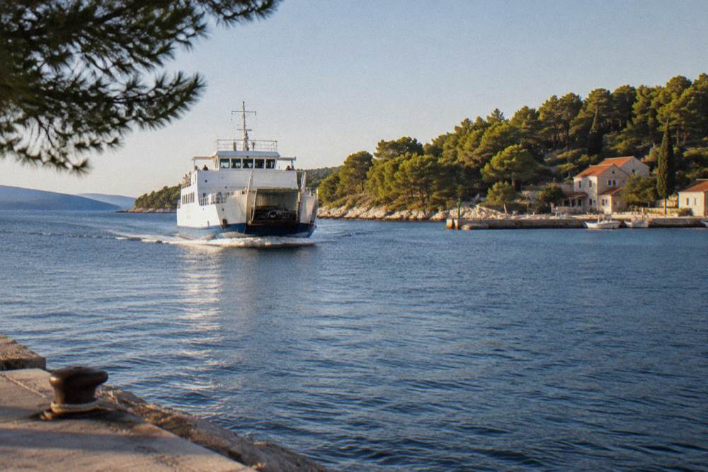 A ferry approaching a small island port with pine trees along the shore