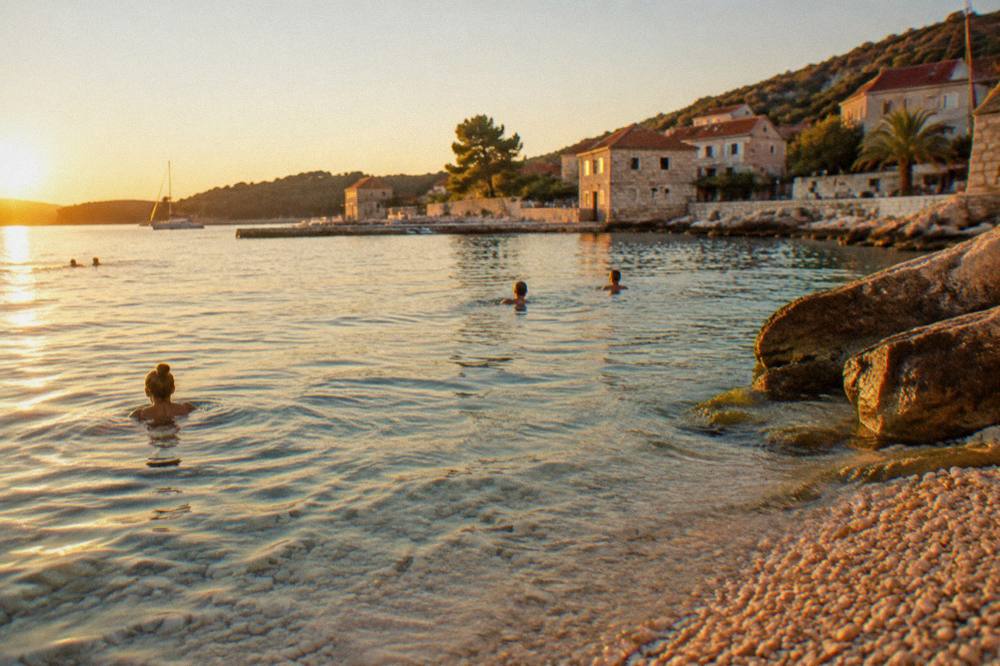 Swimmers in clear shallow water near a pebble shoreline